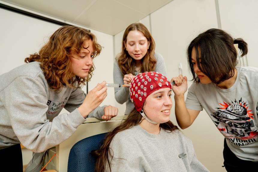 Students standing around another student wearing a red cap for lab 