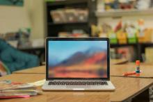 an open laptop rests on a desk at the center of a classroom